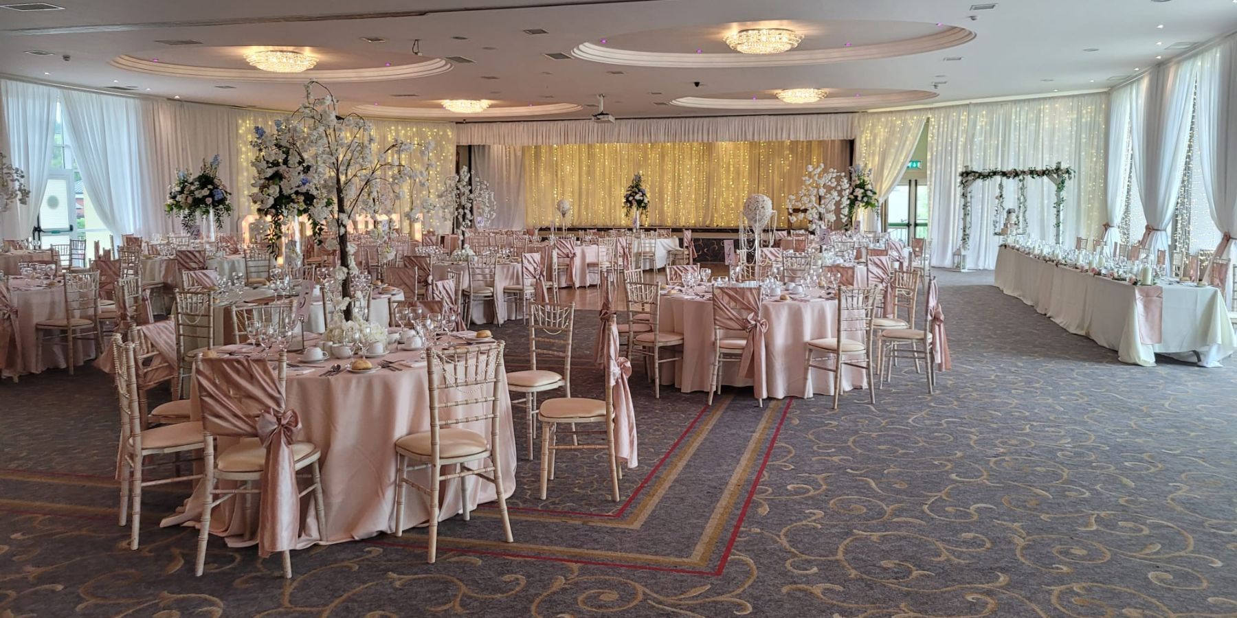 Der atemberaubende Lisfannon-Ballsaal, der von Ultimate Weddings für die Hochzeit von Peter und Rochelle am 9. Juli 2022 ausgestattet wurde. Chivari-Stühle gepaart mit eleganten Drapierungen und romantischen Lichterketten, durchgehend in zartrosa und cremefarbenen Farben.